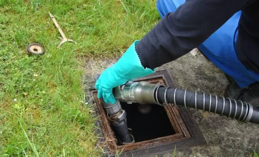 Mains gantées guidant un tuyau d'aspiration dans la trappe d'une cuve à fioul